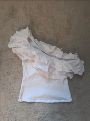 Vit oneshoulder topp med volang - Säljer en vit oneshoulder topp med volanger!🤍