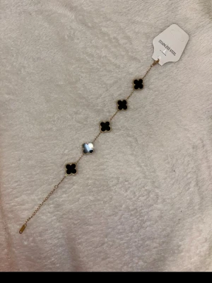 VC armband  - Säljer en snygg väst med svarta blommiga detaljer och guldkant. Västen har en tunn kedja och blommorna är placerade i rad längs hela västen. Materialet är rostfritt stål och designen är riktigt stilren och modern.