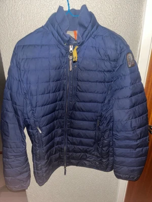 Blå Parajumpers pufferjacka - Säljer en blå pufferjacka från Parajumpers med quiltad design och hög krage. Jackan har flera dragkedjor, inklusive en gul detalj vid halsen och två sidofickor med dragkedja. Insidan är ljusgrå och jackan har långärmade ärmar. Perfekt för kyliga dagar vissa vad du har att erbjuda så kanske vi kan komma överens om ett pris där båda vi två är nöjda 