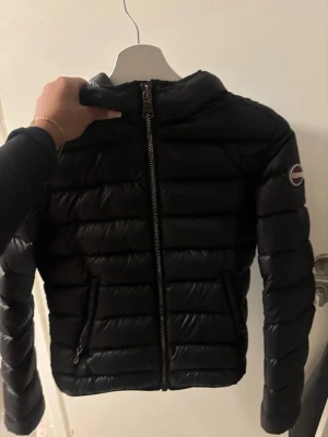 Svart pufferjacka från Colmar - Säljer en svart pufferjacka från Colmar med snyggt quiltad design och dragkedja framtill. Jackan har långärmade ärmar och en rundad krage. Märkeslogga på ena ärmen och praktiska fickor med dragkedja. Perfekt för kyliga dagar!