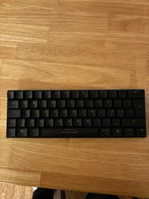 Deltaco Gaming mekaniskt tangentbord - Kompakt mekaniskt tangentbord från Deltaco Gaming med röda switches för snabb respons och tystare användning. Svensk layout, i gott skick utan synligt slitage. Perfekt för gaming och produktivitet. Alla tangenter och switchar ser hela ut. Den är lite smutsig under keycapsen men kan tars bort enkelt. Har andvänt max 4 gånger.