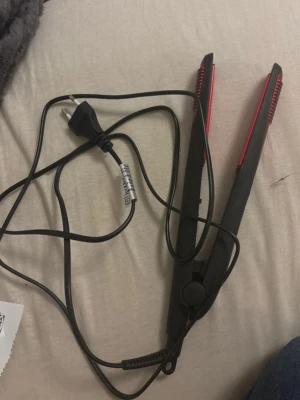 Svart och röd plattång - En svart plattång med röda detaljer och sladd. Perfekt för att styla håret rakt eller skapa lockar. Smidig design som är enkel att använda och passar de flesta hårtyper. Inte 100% säker på om det är rätt märke. PRIS GÅR ATT DISKUTERA!!!!