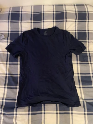 Mörkblå basic t-shirt från H&M - Säljer en mörkblå t-shirt från H&M Basic, tillverkad i mjuk ekologisk bomull. T-shirten har rund hals och korta ärmar, perfekt för en chill och enkel stil. Passformen är normal och tyget känns skönt mot huden.