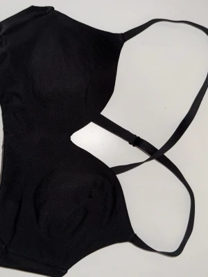 Svart croppad sport topp med smala axelband - Säljer en svart, sport topp med smala justerbara axelband. Toppen  har en enkel och stilren design utan mönster, och är tillverkad i ett mjukt syntetmaterial som sitter bekvämt mot kroppen. Perfekt för att träna i eller använda som en vanlig BH.
