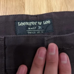 Bruna Leesures by Lee byxor, midja 31 - Säljer ett par bruna byxor från Leesures by Lee med rak passform och klassisk knappgylf. Byxorna har bälteshällor och framfickor, tillverkade i ett slitstarkt bomullsmaterial. Perfekt för dig som gillar retrostil och vill ha något som sticker ut.
