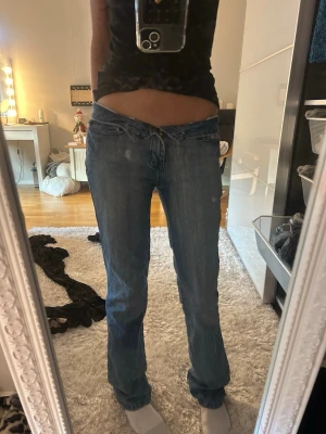 Blå lågmidjade bootcut jeans - Säljer ett par blå jeans med låg midja och bootcut-snitt. Jeansen har klassisk dragkedja och knapp framtill samt broderade detaljer i rosa på bakfickorna. Saknar knappen som man kan se på sista bilden💗