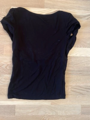 Svart topp med öppen rygg från Gina Tricot - Svart topp från Gina Tricot i storlek S. Modellen har korta ärmar och en öppen rygg. Tunn och mjuk bomullskvalitet som känns skön mot huden. Perfekt att styla med jeans eller kjol för en enkel och snygg look.