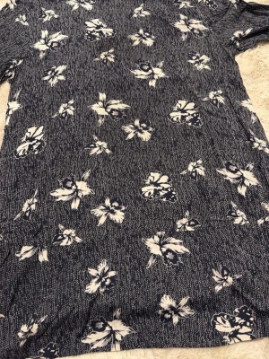 Blommig tunika från Masai XXL - Snygg blå skjorta från Masai i storlek XXL med vitt blommigt mönster över hela plagget. Skjortan har en loose passform och är tillverkad i mjukt och lätt bomullsmaterial. Perfekt för dig som gillar avslappnad stil och coola prints.