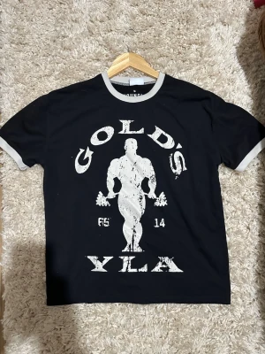 Svart yla T-shirt  - Säljer en svart t-shirt från Gold's Gym . Perfekt för dig som gillar gym. Den  sitter skitbra som lite crop top som ser jävligt bra, är tight på biceps så de ser större ut.
