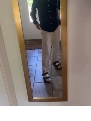 Svarta sandaler med dubbla spännen - Säljer ett par svarta sandaler med två breda remmar och metallspännen. Sandalerna har en platt sula och är perfekta för varma dagar. Materialet ser ut att vara syntet eller skinn och de har en klassisk, enkel design som passar till många olika outfits.