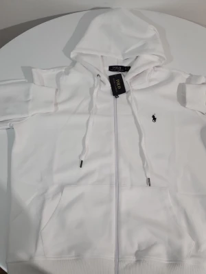 Ralph Lauren zip up  - Säljer en stilren vit zip-up hoodie/tröja från Ralph Lauren i storlek S. Klassisk design med dragkedja framtill och diskret Ralph Lauren-logga på bröstet. Passar perfekt till både vardag och en mer uppklädd stil.