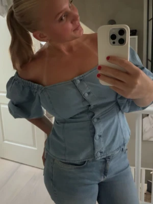 Ljusblå offshoulder korsettopp - Säljer en ljusblå jeanstopp i denim-look med puffiga offshoulder-ärmar och snygga knappar framtill. Man kan ha toppen på lite olika sätt jag valde här att ha den offshoulder. Toppen har figurnära passform och markerad midja, perfekt för dig som vill ha en trendig och cool stil😇🩵🩵