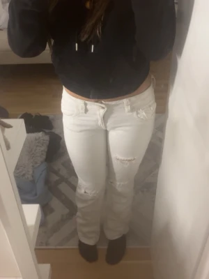 Vita bootcut jeans med slitningar - Säljer ett par vita jeans med bootcut-snitt och snygga slitningar på knäna. Byxorna har låg midja, klassiska fickor fram och bak med knappdetalj på bakfickan. Materialet är jeans och passformen är normal. Perfekt för dig som gillar en fräsch och trendig look.