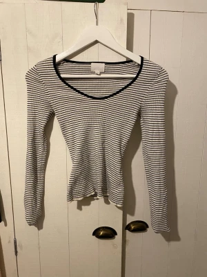 Randig långärmad topp från H&M  - Säljer en ribbad långärmad topp från H&M i storlek XS. Toppen är vit med tunna svarta ränder, har v-ringad halsringning med svart kant och är figurnära i modellen. Perfekt till jeans eller kjol för en enkel men snygg look.
