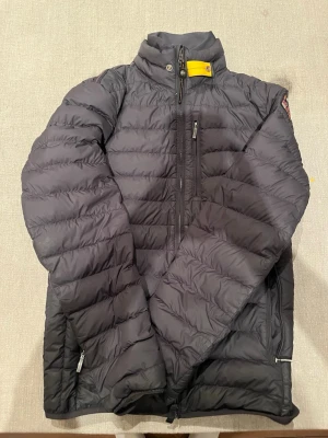 Svart lättviktsdunjacka Parajumpers XS - Säljer en svart superlätt dunjacka från Parajumpers i storlek XS. Jackan har quiltad design, hög krage med gul detalj, dragkedjor framtill och på fickorna samt klassisk Parajumpers-logga på ärmen. Perfekt för kyliga dagar och riktigt snygg passform. Tyvärr har den tre mindre hål som inte märks på avstånd. Ny pris är ca 5000kr.