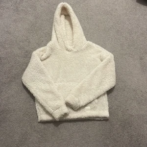 Vit teddyjacka med huva från McKinley - Supermjuk och fluffig vit teddyjacka från McKinley med huva och långärmad design. Perfekt för kalla dagar när du vill vara extra cozy. Jackan har en enkel, clean look och är gjord i gosig fleece som känns skön mot huden.