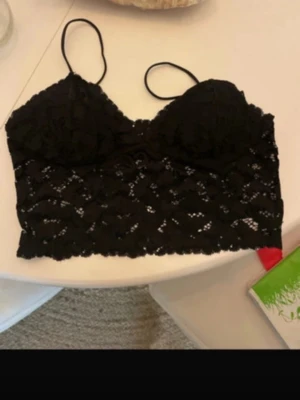 Svart spetsig linnetopp med smala band - Säljer en svart linnetopp med smala axelband och snygg spets över hela toppen. Modellen är croppad och har en feminin look med genombrutet mönster. Perfekt att styla med jeans eller kjol för en cool vibe. den är lite liten i kuporna är storlek L men är mer som en xs s