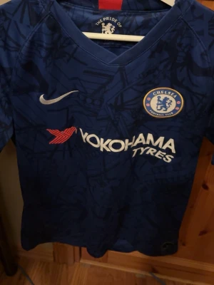 Chelsea FC matchtröja blå Nike - Snygg blå Chelsea FC matchtröja från Nike med klubbmärke på bröstet och Yokohama Tyres som sponsortryck. Tröjan har ett unikt mönster i mörkblått och vit Nike-logga. Perfekt för fotbollsträning eller att bära till vardags om du hejar på Chelsea.