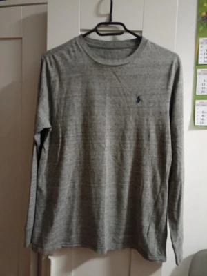 Grå långärmad tröja från Polo Ralph Lauren - Snygg grå långärmad tröja från Polo Ralph Lauren med klassisk rund halsringning och mörkblå broderad logga på bröstet. Tillverkad i mjukt material som känns skönt mot huden. Perfekt till jeans eller chinos för en clean look. M men passar som S