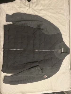 Grå hybridtröja från Moncler - Snygg grå tröja från Moncler med stickade ärmar och quiltad front. Tröjan har hel dragkedja, ribbstickad krage och Moncler-logga på ena ärmen. Perfekt för lager-på-lager och streetstyle. Materialmix av stickat och vadderat tyg. Det är storlek S men passar nog bäst för M. Varan är 1:1 OANVÄND.