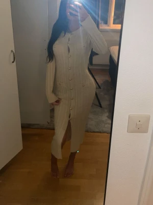 Beige ribbad långklänning med knappar - Säljer en beige ribbad långklänning med långa ärmar och knappar hela vägen framtill. Klänningen har en slits nedtill och markerade fickor vid höfterna. Perfekt för dig som gillar en stilren och elegant look.