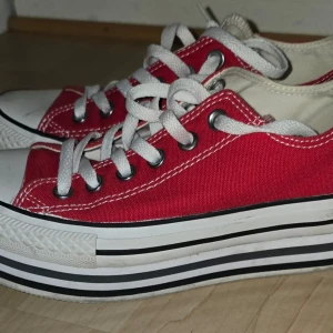 Röda Converse All Star sneakers - Klassiska röda Converse All Star sneakers med hög vit gummisula och svarta ränder. Låga i modellen med vita skosnören och silverfärgade öljetter. Ovandel i canvas och tåhätta i vitt gummi. Perfekta för en cool och avslappnad stil.