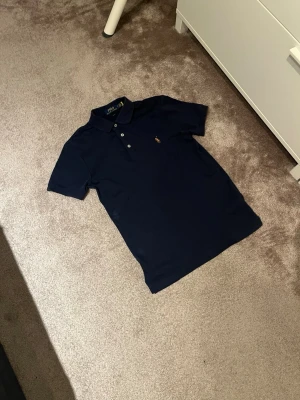 Ralph lauren piké - Säljer en mörkblå Ralph lauren piké i mycket bra skick. Pikén är k storlek S men sitter som xs