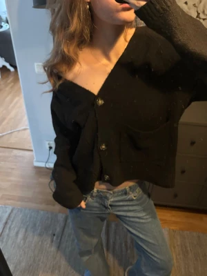 Svart croppad kofta med knappar - Säljer en svart croppad kofta med stora knappar framtill och två fickor. Koftan är i gott skick!