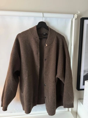 Brun kofta från Lindex, M - Mysig brun kofta från Lindex med knappar framtill och två stora fickor. Koftan har ribbstickad krage och muddar vid ärmslut och nederkant. Perfekt för lager på lager och enkel att matcha🙌🏼andvänd fåtal gånger