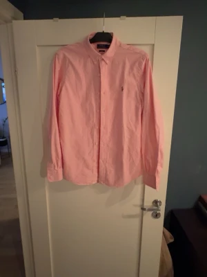 Rosa skjorta från Ralph Lauren - Klassisk rosa skjorta från Ralph Lauren med button-down krage och broderad logga på bröstet. Skjortan har lång ärm och knäppning framtill. Perfekt för en stilren och avslappnad look.