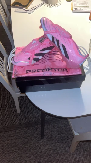 Adidas Predator Beckham rosa fotbollsskor - Säljer ett par Adidas Predator fotbollsskor i en riktigt snygg rosa färg med svarta detaljer och vita sulor. Skorna har Beckham-tryck och klassiska tre ränder på sidan. Tillverkade i syntetmaterial och levereras med matchande rosa påse och originalkartong. Kom med förslag på byten!