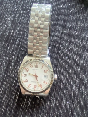 Reginald silverfärgad armbandsklocka - Stilren armbandsklocka från Reginald med silverfärgat metallarmband och vit urtavla. Klockan har röda siffror, datumvisning och en räfflad kant runt urtavlan. Perfekt accessoar för dig som gillar klassisk design med en modern touch.