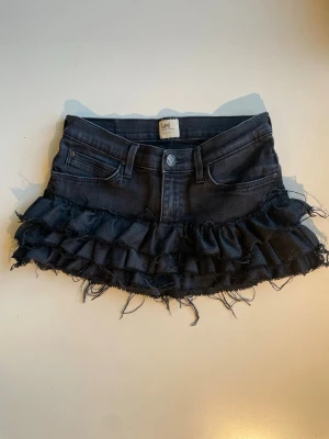 Svart volangkjol - Supersnygg svart jeanskjol med volangdetaljer och råa kanter. Kjolen har klassiska fickor fram och bak samt bälteshällor. Har sytt den från ett par gammla Lee jeans. Det står ingen storlek på men skulle säga att den är XS. Midjemått: 32 cm  Längd: 25 cm. Skriv om ni hr frågor!🖤