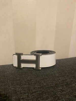 Vitt skärp med H-spänne - Snyggt vitt skärp från med det ikoniska H-spännet i silverfärgad metall. Bältet har en stilren, klassisk design som lyfter vilken outfit som helst.