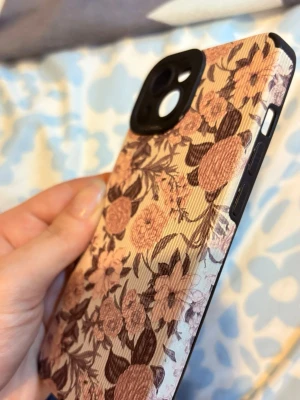 Blommigt mobilskal i rosa och beige - Snyggt mobilskal med blommigt mönster i rosa och beige toner. Skalet har en matt, lätt räfflad yta och svarta detaljer runt kameran. Passar perfekt för dig som vill ha en stilren och trendig look på mobilen.