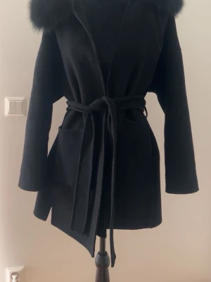 Svart kappa med fuskpäls och knytskärp - Svart elegant kappa i oversized modell med bälte i midjan och mjuka pälsdetaljer på axlarna. Väldigt stilren och perfekt till höst/vinter. Passar perfekt till både vardag och finare tillfällen. 💕  • Storlek: XS (passar även S pga oversized passform) • Färg: svart • Skick: använd men i väldigt fint skick • Nypris: ca 3000 kr