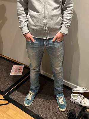 Blå Nudie Jeans, W28 L30 - Säljer ett par klassiska blå jeans från Nudie Jeans med snygg slitning och kontrastsömmar. Modellen har raka ben och normal passform. Tillverkade i slitstarkt bomullstyg och perfekta för dig som gillar en avslappnad men ändå stilren look. De är kapade från L32-L30 W28