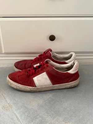 Röda Valentino Flycrews - Snygga sneakers från Valentino i rött och vitt mocka med klassisk låg siluett. Skorna har röda snören, vit panel på sidan och en robust yttersula. Perfekta för dig som vill ha en stilren men ändå färgstark look.