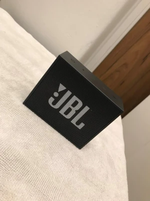 JBL Go svart trådlös högtalare - Smidig och portabel svart JBL Go trådlös högtalare med tydlig JBL-logga på framsidan. Rektangulär design i plast och metallgaller, perfekt för att spela musik via Bluetooth. Laddas enkelt med medföljande USB-kabel.