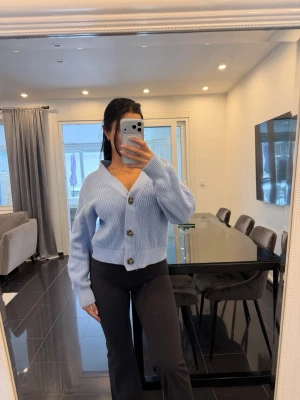 Ljusblå ribbstickad kofta - Trendig ljusblå kofta med stora knappar framtill och ribbstickat material. Koftan har en djup V-ringning och långa ärmar med breda muddar. Perfekt för lager-på-lager och ger en chill vibe till din outfit.