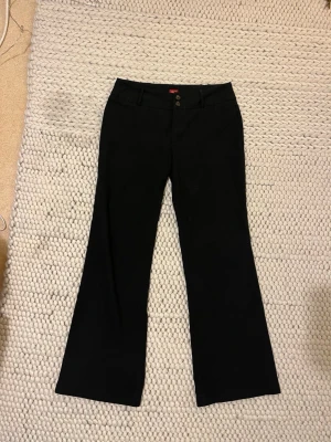 Svarta kostymbyxor från Esprit - Stilrena svarta kostymbyxor från Esprit med bootcut-snitt och två knappar i midjan. Byxorna har klassisk passform och är perfekta för en dressad look. Materialet känns mjukt och följsamt, och färgen är helsvart. 42 men passar också 40/38