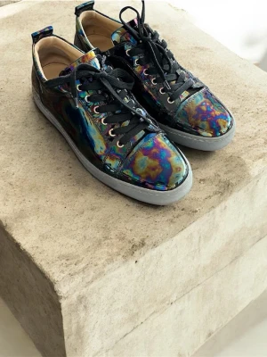 Christian Lobutin Louis oslick patent - Unika lobus  med iriserande, glansig yta i flera färger och svart snörning. Skorna har genomskinliga platt sula och rund tå. Insidan är beige och materialet ser ut att vara syntet eller skinn. Perfekta för dig som vill sticka ut med din stil. Gör som ingen annan ha bara din stil ✨nypris: 7500