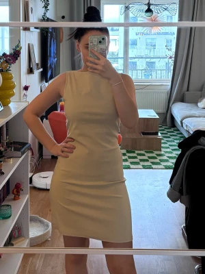 Beige ärmlös kortklänning med knyt - Snygg beige kortklänning med ärmlös design och rund halsringning. Klänningen har ett knyt i midjan som ger en fin siluett. Perfekt för dig som gillar stilrena och enkla plagg med en twist. På grund av snöre på ryggen så kan man själv bestämma hur tajt vill man ha klänning. Fin för sommaren eller för någon fest. Köpte den från Hissy Fit. 