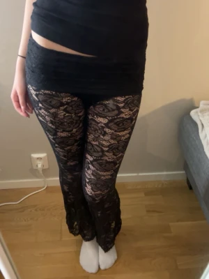 Svarta lågmidjade spetsbyxor med utsvängda ben - Säljer dessa svarta spetsbyxor som aldrig använts❤️ De har inbyggda shorts och är i storlek XS/34. Har sprättat upp längst ner för att de var för korta för mig men annars är de i bra skick.