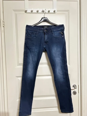Replay Anbass mörkblå jeans  - Säljer ett par Replay Anbass jeans i mörkblå tvätt med klassisk femficksdesign och snygga detaljer på bakfickorna. Jeansen har raka ben och normal passform, tillverkade i mjukt och slitstarkt bomullsmaterial med lite stretch för extra komfort. Storlek finns på sista bilden.