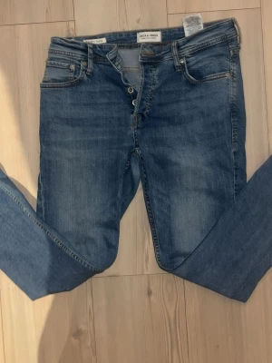 Blå slim fit jeans Jack & Jones - Säljer ett par blå slim fit jeans från Jack & Jones med klassisk femficksdesign och knappgylf. Jeansen har en snygg tvättad look och är tillverkade i bomull med lite stretch för extra komfort.