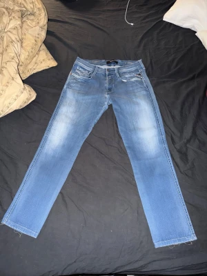Blåa Replay anbass 33-29 - Snygga blå jeans från Replay med raka ben och klassisk femficksdesign. Jeansen har ljusa slitningar framtill och logotypdetalj på myntfickan. Perfekta för en avslappnad och trendig look. Släppt lite i summorna nere vid fötterna annars fint skick! Skriv vid frågor, snabb leverans🚚