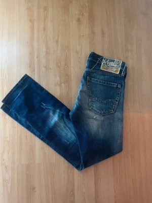 Blåa Replay jeans med slitningar - Snygga blå jeans från Replay med tydliga slitningar och tvättade detaljer. Klassisk femficksmodell med raka ben och låg midja. Jeansen har en cool vintage-look och är tillverkade i bomull. Perfekta för en avslappnad streetstil. Detta går ej att köpa i butik och slitningarna är gjorde vid proffs