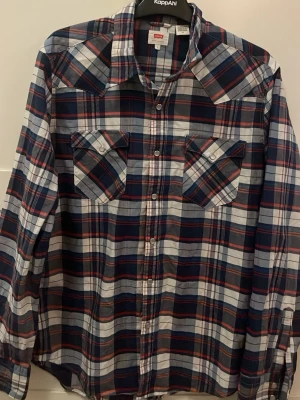 Rutig skjorta från Levi's blå/röd - Snygg rutig skjorta från Levi's i blått, rött och vitt. Klassisk westernmodell med två bröstfickor och tryckknappar. Perfekt för en avslappnad stil och passar till jeans eller chinos. Skjortan har lång ärm och mjukt bomullstyg.
