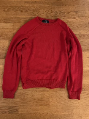 Röd stickad tröja från Human scales - Säljer en enkel och snygg röd stickad tröja från Humanscales. Tröjan har rund halsringning, ribbade muddar vid ärmslut och nederkant samt en klassisk rak passform. Perfekt för dig som gillar stilrena plagg i starka färger.